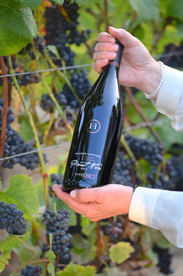 A bottle of Double-Gold Clone 828 in the vineyard covered in grape clusters for our next vintage.